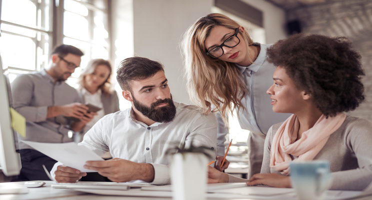 Due donne e un uomo dialogano in ufficio ed esaminano documenti e report