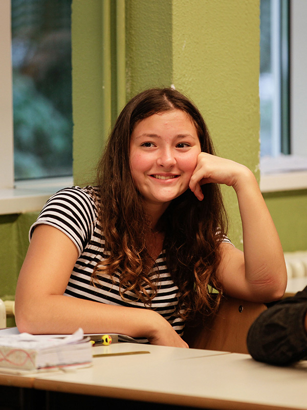 Primo piano di una studentessa della scuola secondaria di primo grado, seduta in classe che sorride.