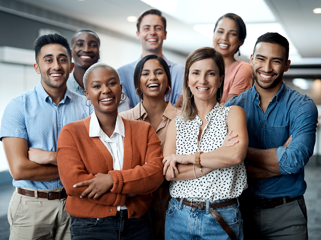 Gruppo di giovani professionisti e professioniste di background culturali diversi che sorride all’interno di spazi aziendali.