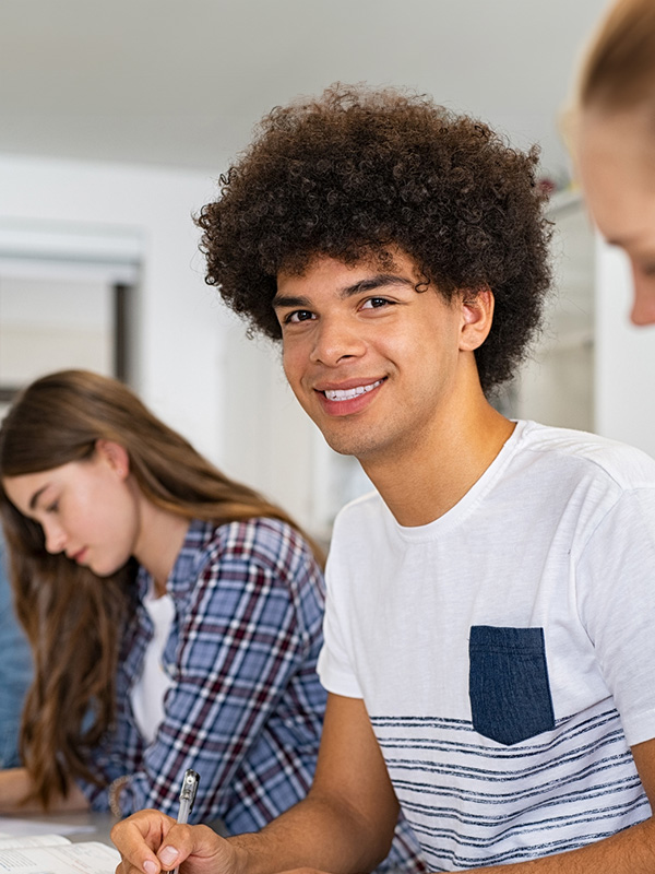 Primo piano di uno studente della scuola secondaria di secondo grado, seduto in classe che sorride.