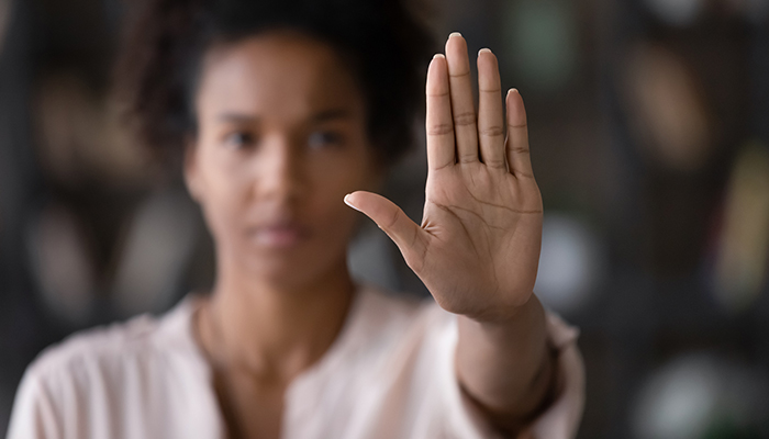 Primo piano della mano alzata di una professionista, simbolo di stop ai pregiudizi per background culturali diversi in azienda.​