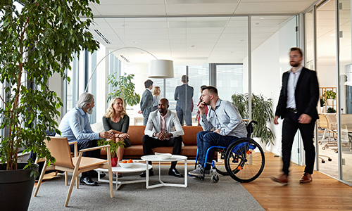 Gruppo di persone di background diversi e con disabilità che si confronta all’interno degli spazi aziendali.