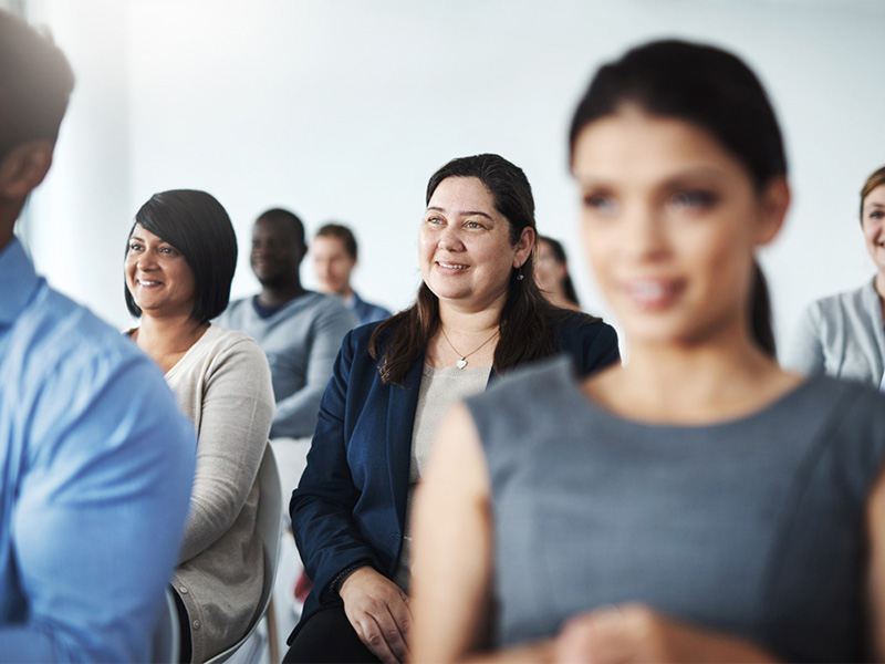 Gruppo di professioniste e professionisti seduti a una riunione del board in azienda, sorridenti.