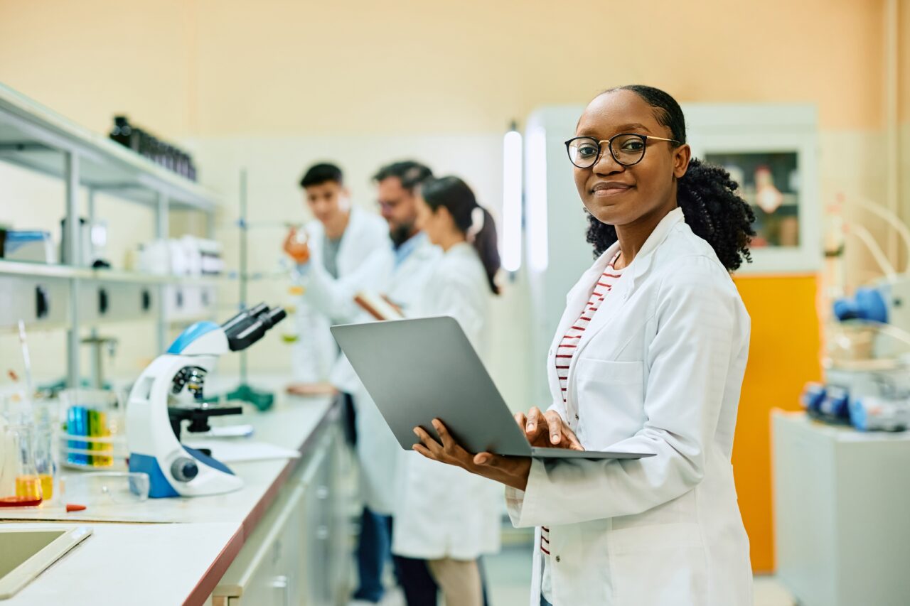 Giovane scienziata nera con computer in mano che lavora in un laboratorio