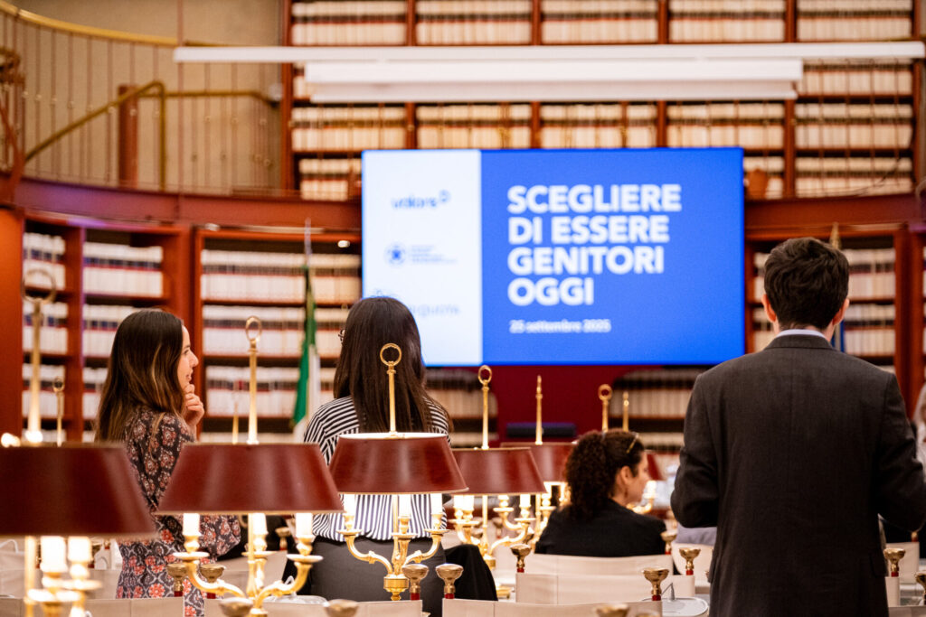 Foto della Biblioteca "Nilde Iotti" Camera dei Deputati. Persone di spalle guardano una slide proiettata con scritto il titolo dell'incontro "Scegliere di essere genitori oggi", un evento su genitorialità, cura e conciliazione vita-lavoro.