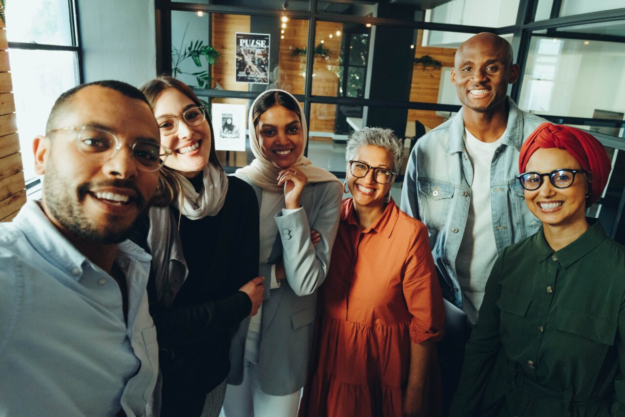Donne e uomini di etnie e culture diverse in gruppo sorridenti si scattano un selfie all'interno di un ufficio
