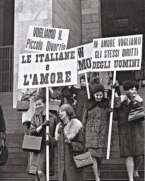 Foto d'epoca che ritrae una manifestazione femminista a favore dell'introduzione del divorzio in Italia, in cui diverse donne vestite con abiti e pettinature d'epoca tengono in mano dei cartelloni con scritto "Le italiane e l'amore", "In amore vogliamo gli stessi diritti degli uomini"
